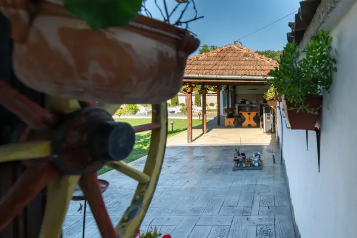Каруцарско колело и саксии с цветя на стената край плочника